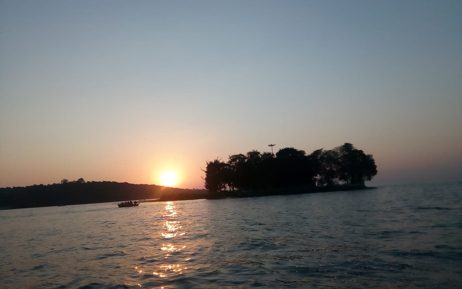 Sunset over the Upper Lake in Bhopal, with a small wooded island and a boat in silhouette